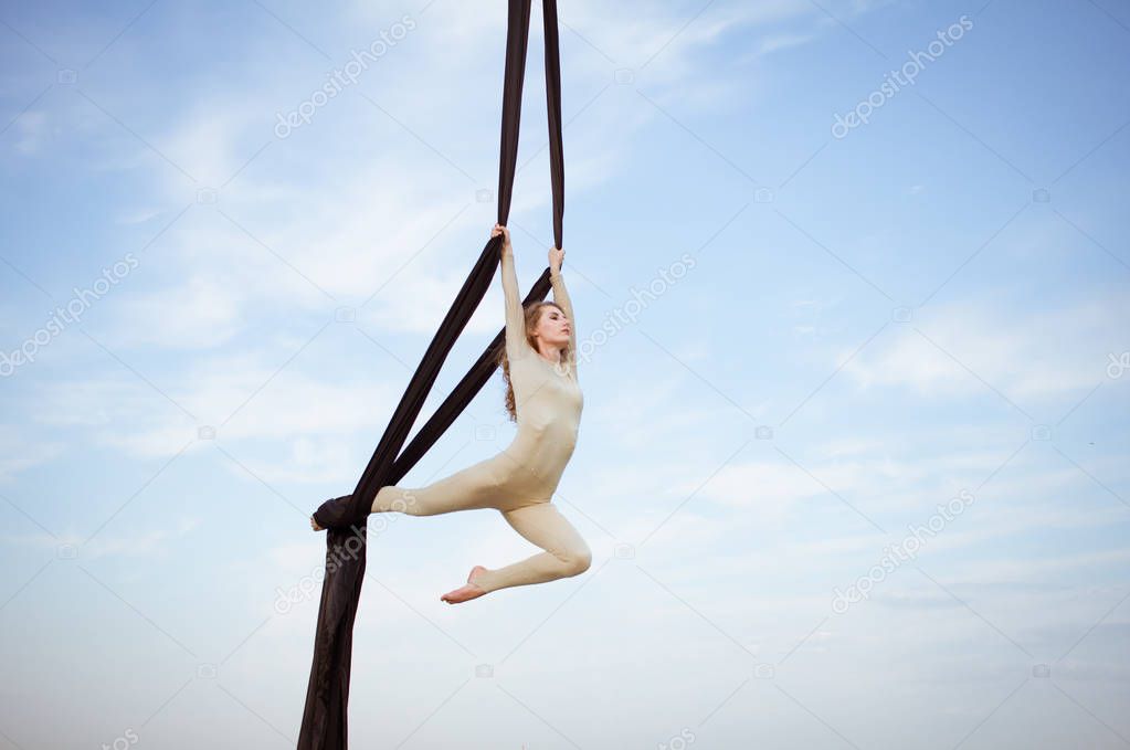 Fit woman in skinny skinny clothes dancing with aerial silk on a sky background, gymnast training on aerial silk