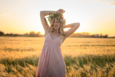 kafası güzel sarışın Bayan çiçek çelenk gündoğumu sırasında yaz buğday alanlarında