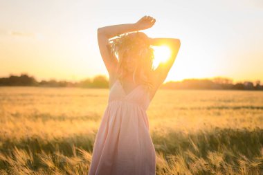 kafası güzel sarışın Bayan çiçek çelenk gündoğumu sırasında yaz buğday alanlarında