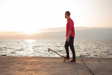 Kırmızı gömlek ve mavi jeans sahil yakınında longboard üzerinde sürme sırasında gündoğumu, deniz ya da okyanus arka plan patenci