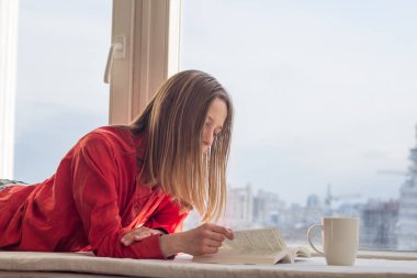 Genç kadın relzxing kitap ve kahve ya da çay pencere pervazına portresi