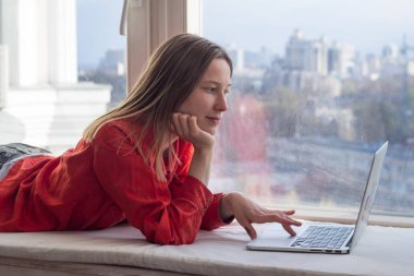 Pencere pervazına, beyaz famele dizüstü kullanarak oturan dizüstü bilgisayar ile yuong güzel kadın