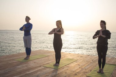 Grup insanlar yoga teşkil stand ahşap iskele üzerinde içinde belgili tanımlık deniz geçmiş gündoğumu