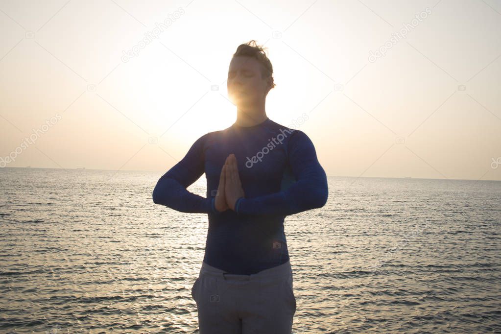 Young man doing yoga in the beach. Morning sea background.