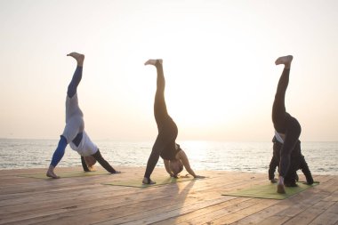 Grup insanlar yoga teşkil stand ahşap iskele üzerinde içinde belgili tanımlık deniz geçmiş gündoğumu