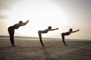 Genç kadınlar Yoga uygulamak pozlar ve asanas. Ortak yoga akrobatik yoga. Çölde siyah giymek eğitim gün batımı sırasında yoga sınıfında