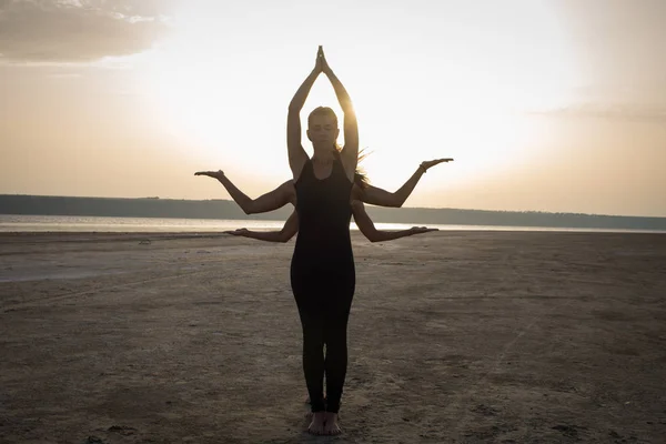 young women practicing yoga poses and asanas. Partner yoga, acrobatic yoga. Yoga class in black wear training in desert during sunset