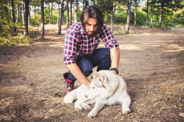 Genç hipster siyah kot pantolon deri çizmeler ve gömlek yürümek orman ile Sibirya husky köpek