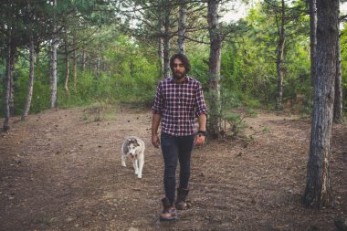 Genç hipster siyah kot pantolon deri çizmeler ve gömlek yürümek orman ile Sibirya husky köpek