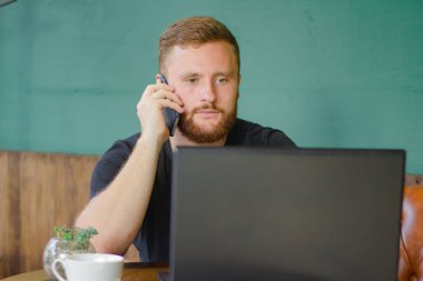 Genç sakallı Kızıl saçlı erkek iş cep telefonu ve laptop ile Cafe