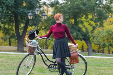 Sonbahar parkta genç kadın kitap, güzel kızıl saçlı kadın yeşil çimenlerin üzerinde bisiklet ile okumak