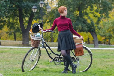 Sonbahar parkta genç kadın kitap, güzel kızıl saçlı kadın yeşil çimenlerin üzerinde bisiklet ile okumak