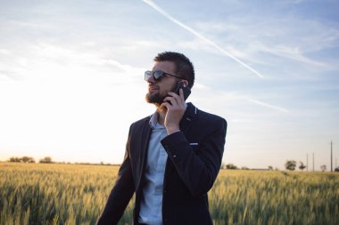 Siyah takım elbise speacking telefon güzel gün batımı sırasında buğday alanında genç adam