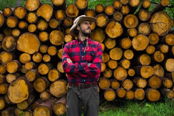 森林中木材手的肖像 许多大原木的松树的背景 在松林的锯木附近摆姿势的年轻男性徒步者 — 图库照片