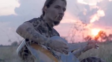 güzel gün batımı sırasında oung dövmeli erkek oyun yaz alanlardaki akustik gitar