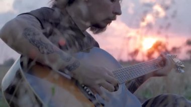 güzel gün batımı sırasında oung dövmeli erkek oyun yaz alanlardaki akustik gitar