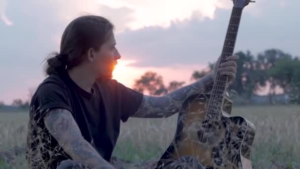オーン入れ墨美しい日没時に夏フィールドでアコースティック ギターの雄プレイ — ストック動画