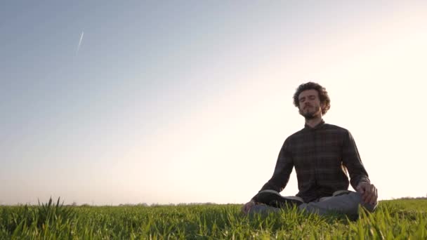 夕日や日の出に対して男性の瞑想の後緑の野原でリラックスしたカジュアルな服装の若い男 — ストック動画