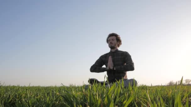 夕日や日の出に対して男性の瞑想の後緑の野原でリラックスしたカジュアルな服装の若い男 — ストック動画