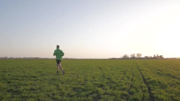 若い選手は夕日や日の出に対して緑のスプリング フィールドで実行 — ストック動画