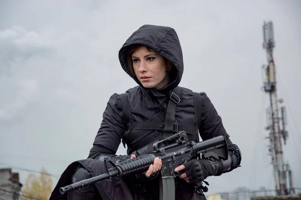 Genç kadın modern siyah techwear tarzı tüfekle poz çatı, Kızıl saçlı kadın cyperpunk veya sonrası kıyamet kavramı portresi
