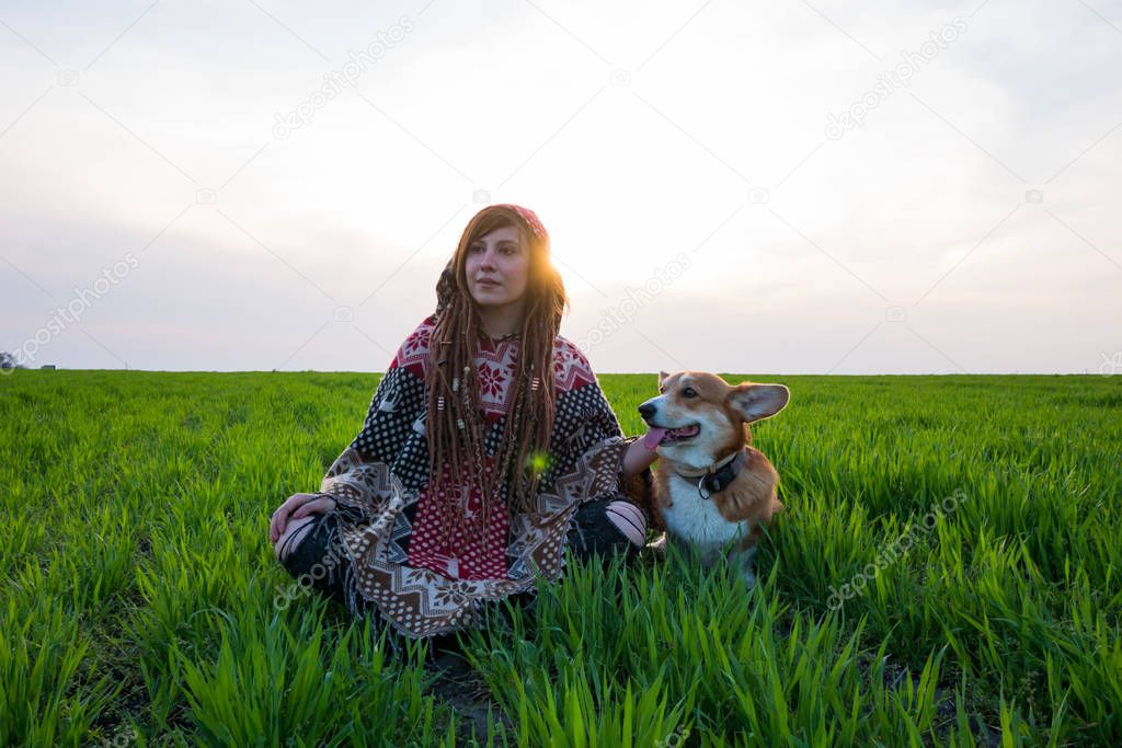 Young woman in poncho with corgi dog relaxing in the spring fields