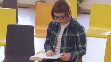 Gözlük Genç Redhead kadın kütüphanede kitap okumak