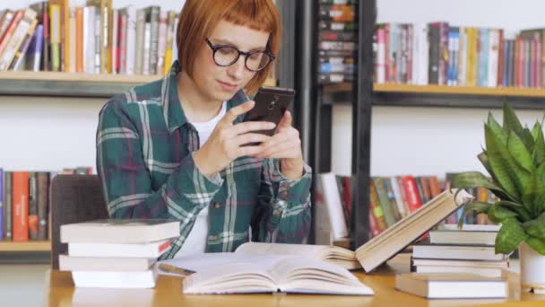 Молодая Рыжая Женщина Очках Читает Книги Библиотеке — стоковое видео