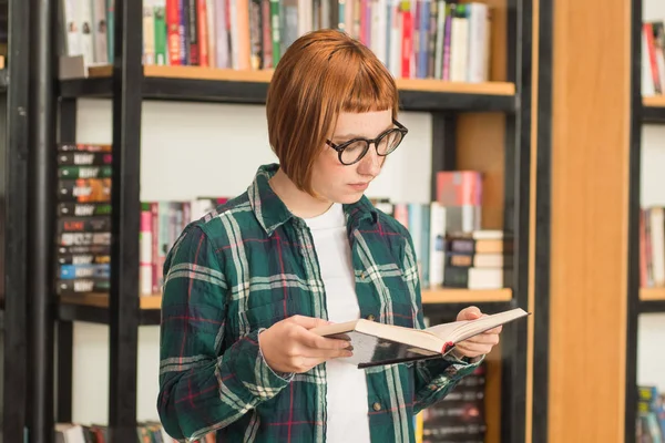 Młoda Ruda Kobieta Okularach Czytać Książkę Bibliotece — Zdjęcie stockowe