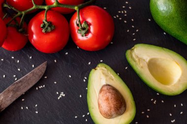 Domates ve avokado siyah masada yakın, renkli sağlıklı gıda 
