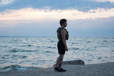 Genç sakallı atlet ağırlıklı yelek ile açık havada eğitim, askeri plaka taşıyıcı ile egzersiz