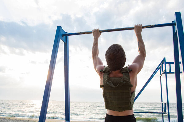 Young bearded athlete training outdoor with weighted vest,  exercise with military plate carrier