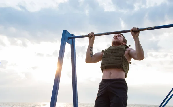 Young bearded athlete training outdoor with weighted vest,  exercise with military plate carrier