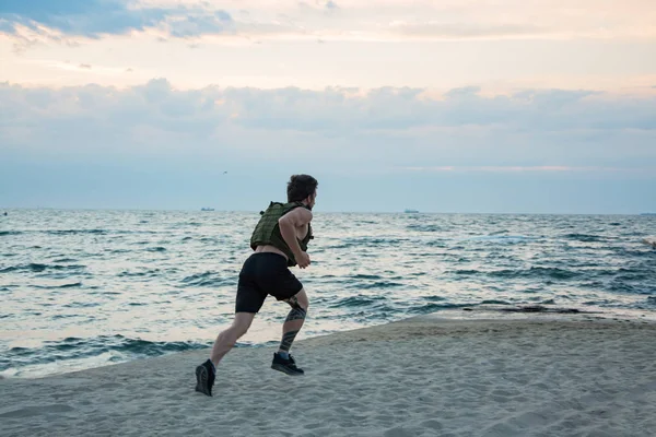 Young bearded athlete training outdoor with weighted vest,  exercise with military plate carrier