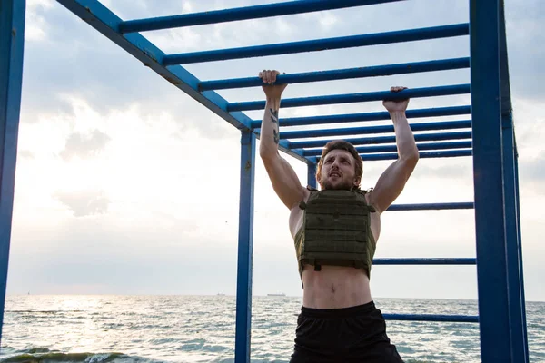 Young bearded athlete training outdoor with weighted vest,  exercise with military plate carrier