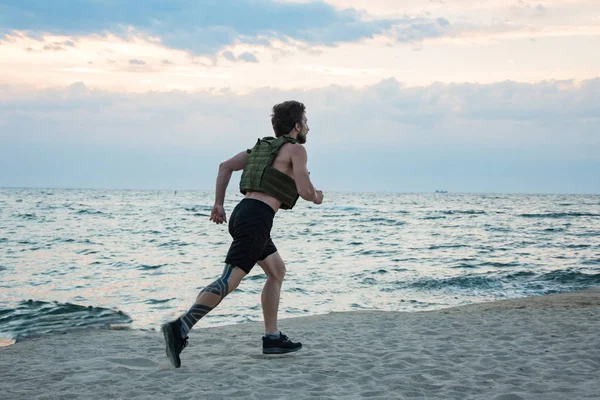 Young bearded athlete training outdoor with weighted vest,  exercise with military plate carrier