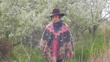 Genç kadın gezgin poncho ve şapka alanları ve çiftlikte yürümek