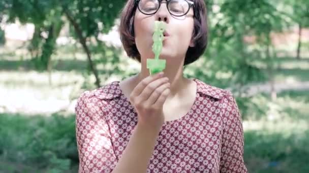 戴着眼镜的年轻女子在公园里户外吹泡泡 — 图库视频影像