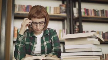 Gözlük Genç Redhead kadın kütüphanede kitap okumak