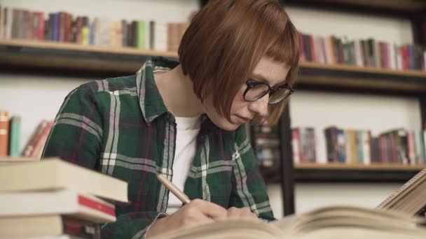 Joven Pelirroja Gafas Leer Libro Biblioteca — Vídeos de Stock