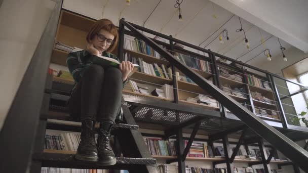Junge Rothaarige Frau Mit Brille Liest Buch Der Bibliothek — Stockvideo