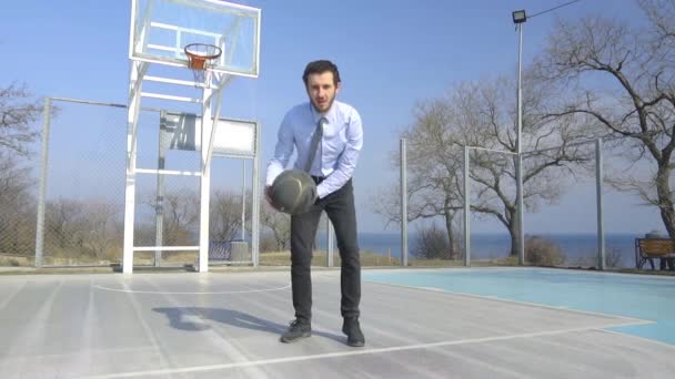 晴れた日に屋外で一人でバスケットボールをするスーツとネクタイの若いビジネスマン — ストック動画