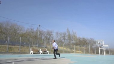 Takım elbiseli ve kravatlı genç iş adamı güneşli bir günde açık havada tek başına basketbol oynuyor