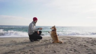 Genç erkek sonbaharda sahilde corgi köpek ile oynamak