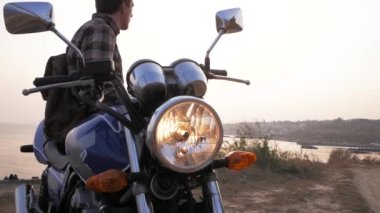 Yonk erkek gezgin, güzel gün batımında deniz kenarında motosikletin üzerinde oturuyor. 
