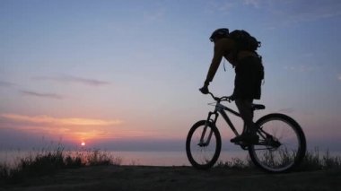Deniz kenarında dağ bisikleti süren erkek güzel gün batımına karşı 