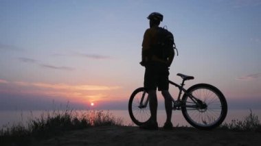 Deniz kenarında dağ bisikleti süren erkek güzel gün batımına karşı 