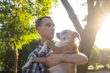 Mutlu genç erkek, yaz güneşli parkta cinsiyetsiz köpekle oynuyor.