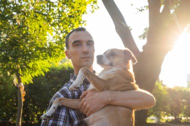 Mutlu genç erkek, yaz güneşli parkta cinsiyetsiz köpekle oynuyor.