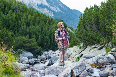 Pançolu ve sırt çantalı genç bayan gezgin büyük kayalıklarda duruyor.